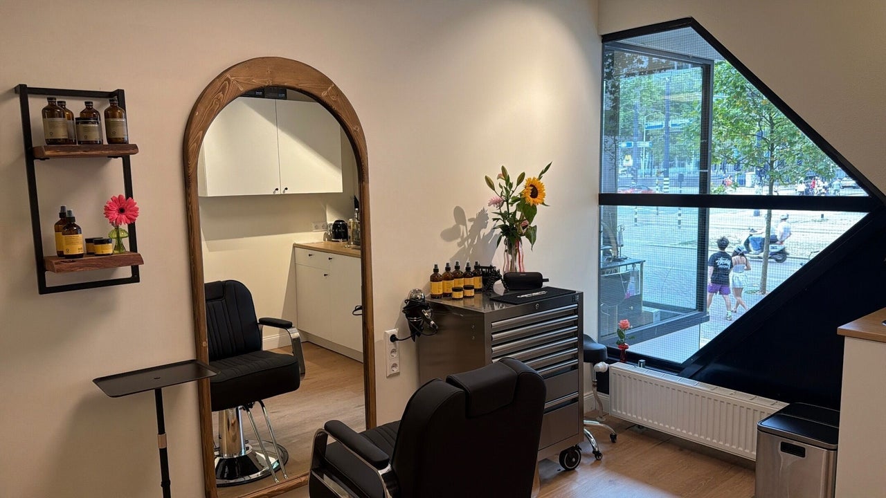 De studio van JAM.IN: boogspiegel van hout, zwarte kappersstoel en het grote schuine raam